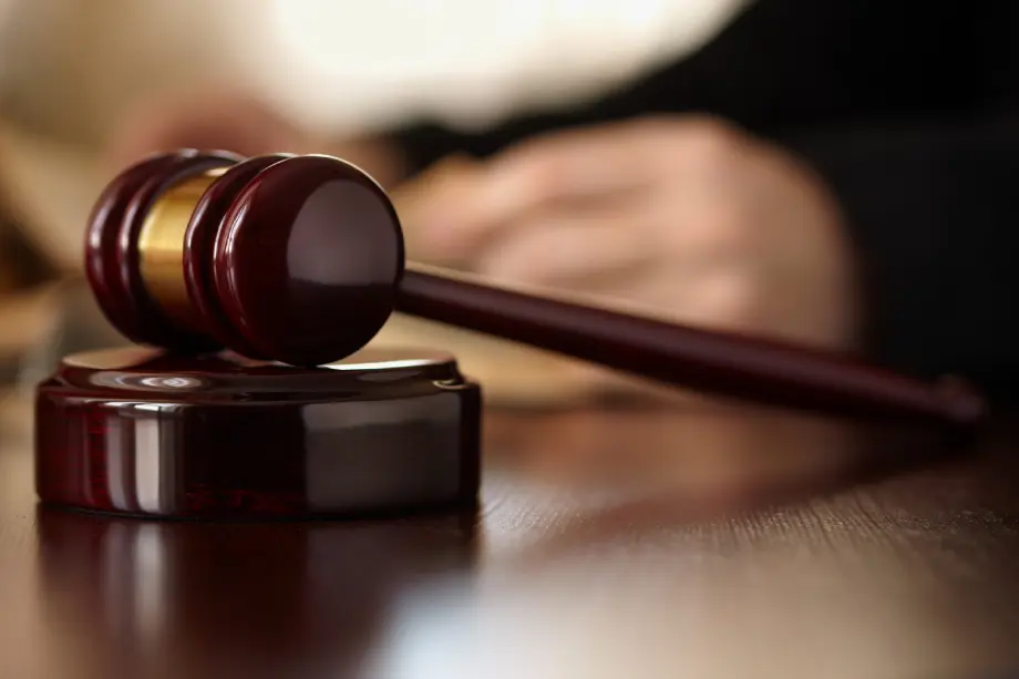 A wooden gavel rests on a sound block with a blurred person in the background.