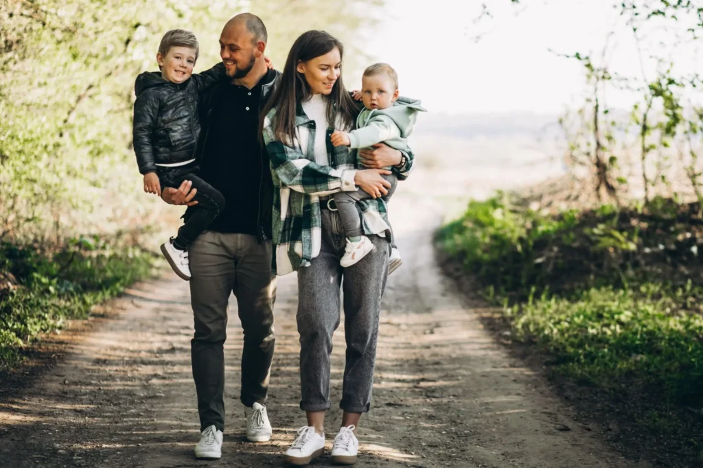 A family of four walks on a dirt path outdoors, enjoying time together. Estate planning for young families ensures their loved ones are protected as they create memories among the trees and greenery lining the path.
