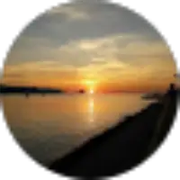 A blurry photo of a sunset over a calm body of water, with the sun low on the horizon and clouds in the sky.